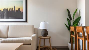 A living room with a sofa, a lamp on a stool, a potted plant, and a framed picture on the wall.