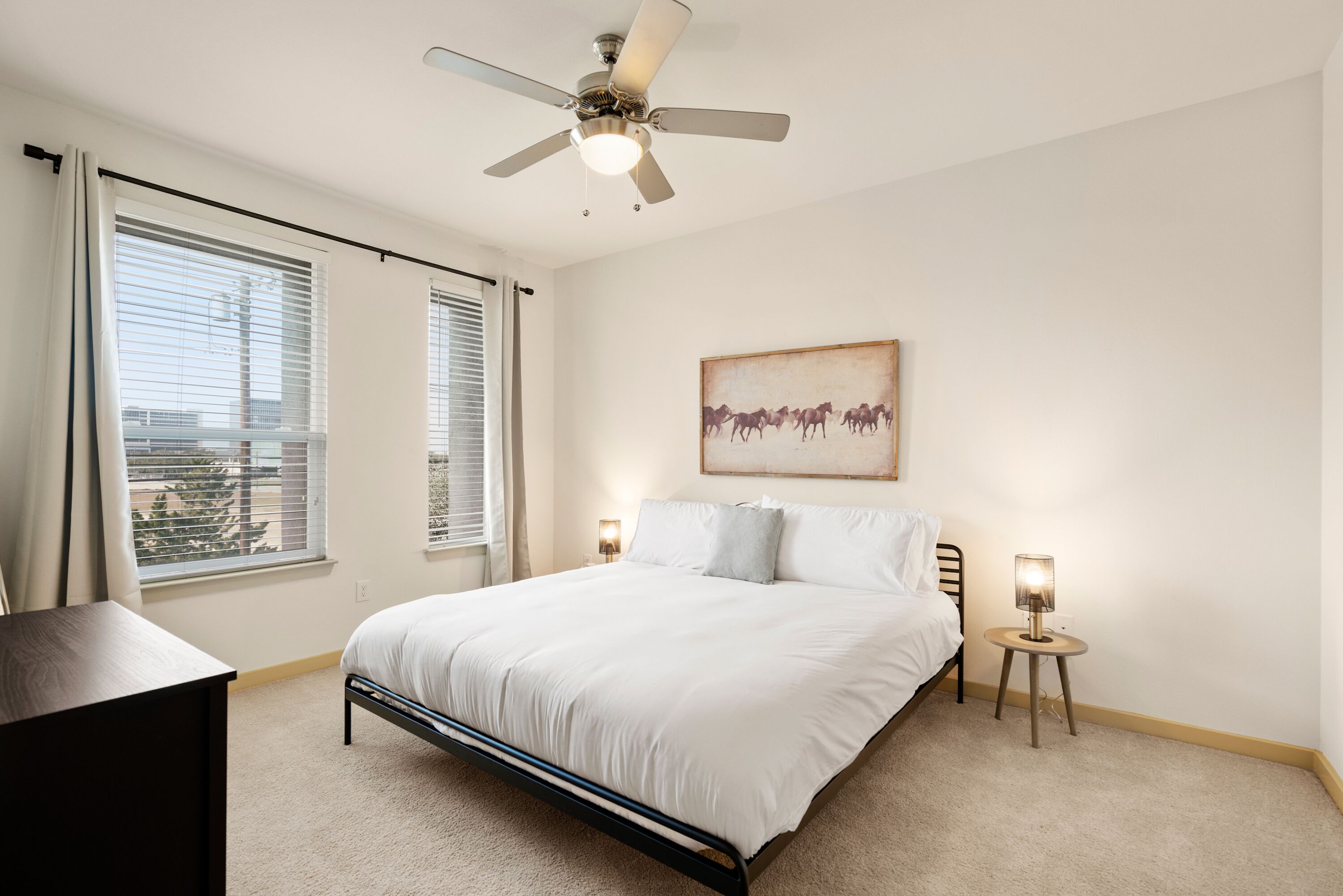 A bedroom with a bed, two bedside lamps, a ceiling fan, and a window with blinds.