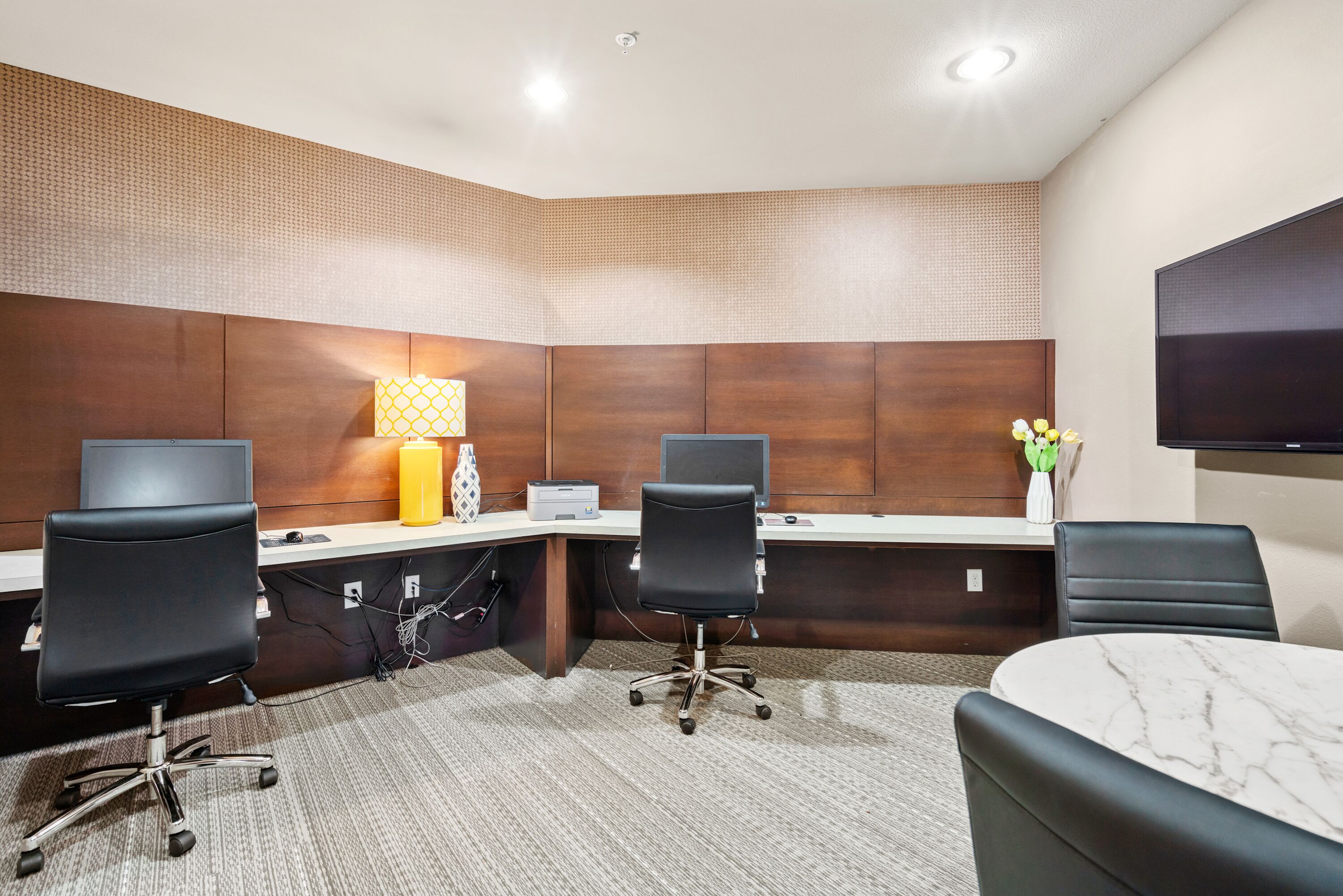 A hotel room with a desk, two office chairs, a TV, and a bed.