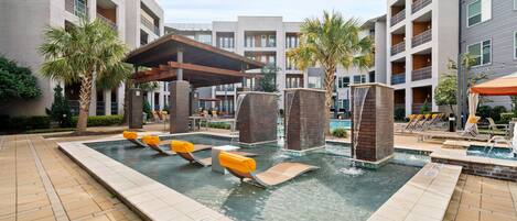 A pool area with lounge chairs, a water feature, and a covered seating area.
