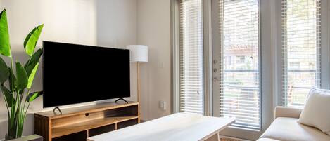 A modern living room with a flat-screen TV on a wooden stand, a white sofa, a coffee table, and a large plant.