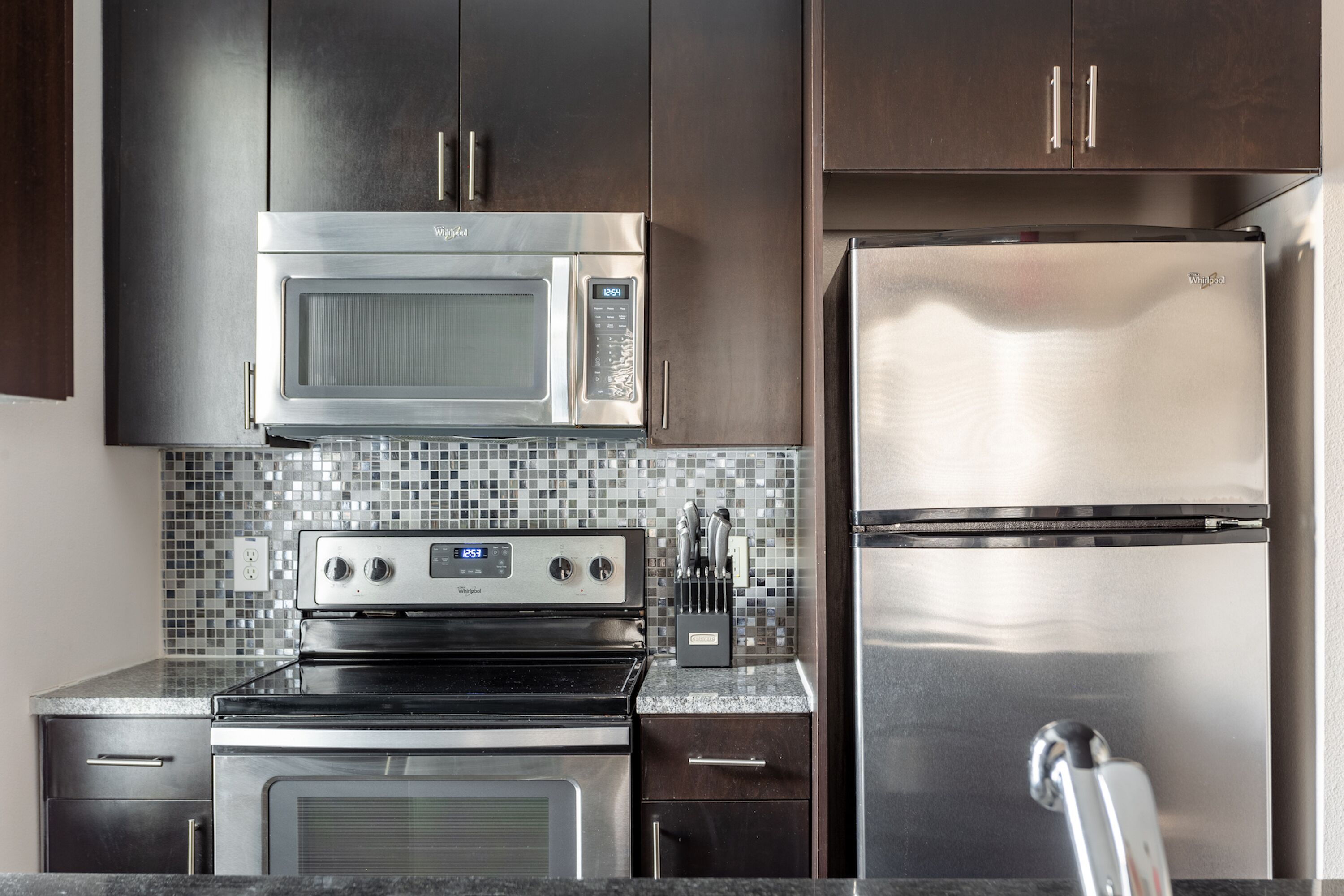 Una cocina moderna con electrodomésticos de acero inoxidable, gabinetes de madera oscura y salpicadero de azulejos.