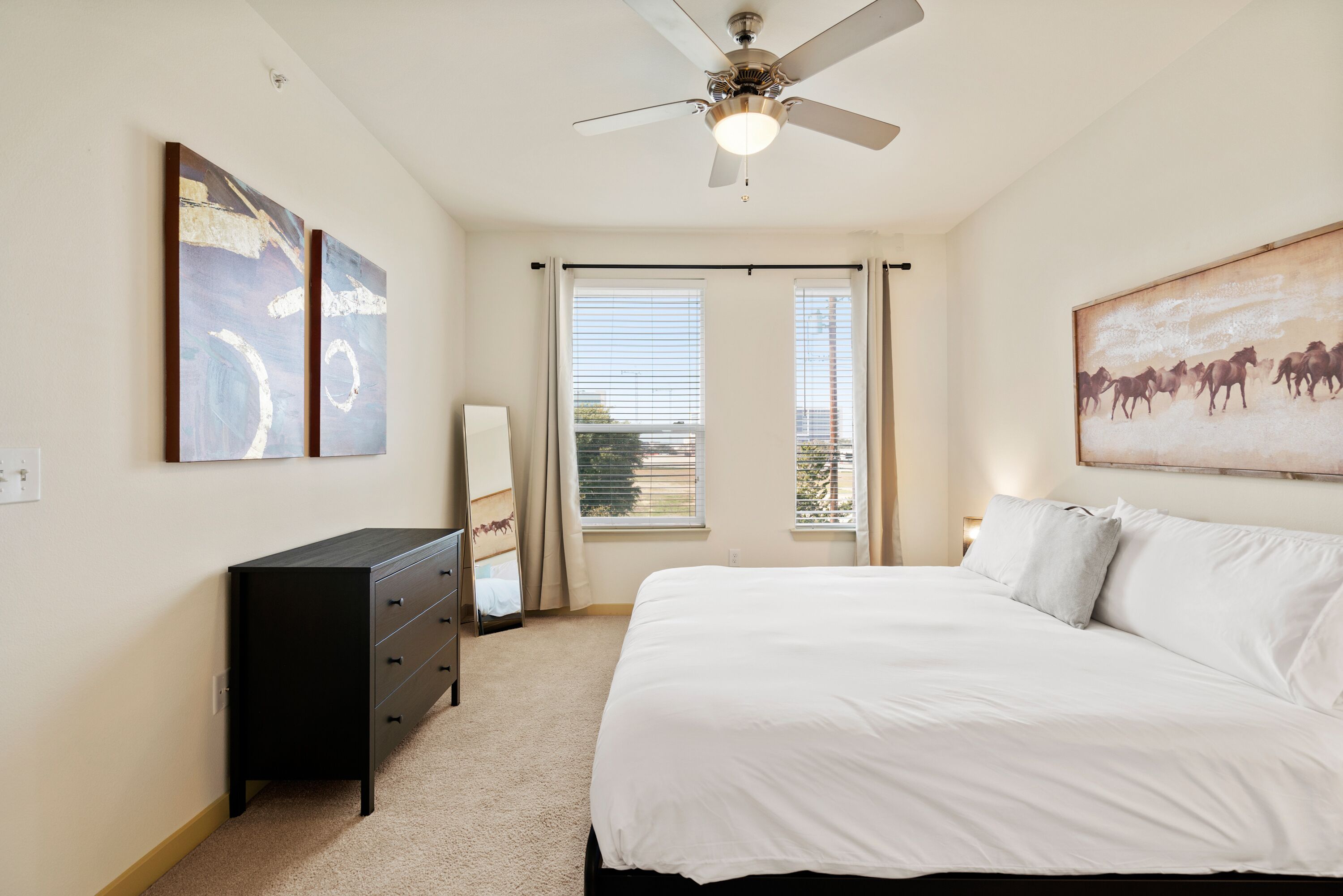 A bedroom with a bed, a dresser, a ceiling fan, and a window with curtains.