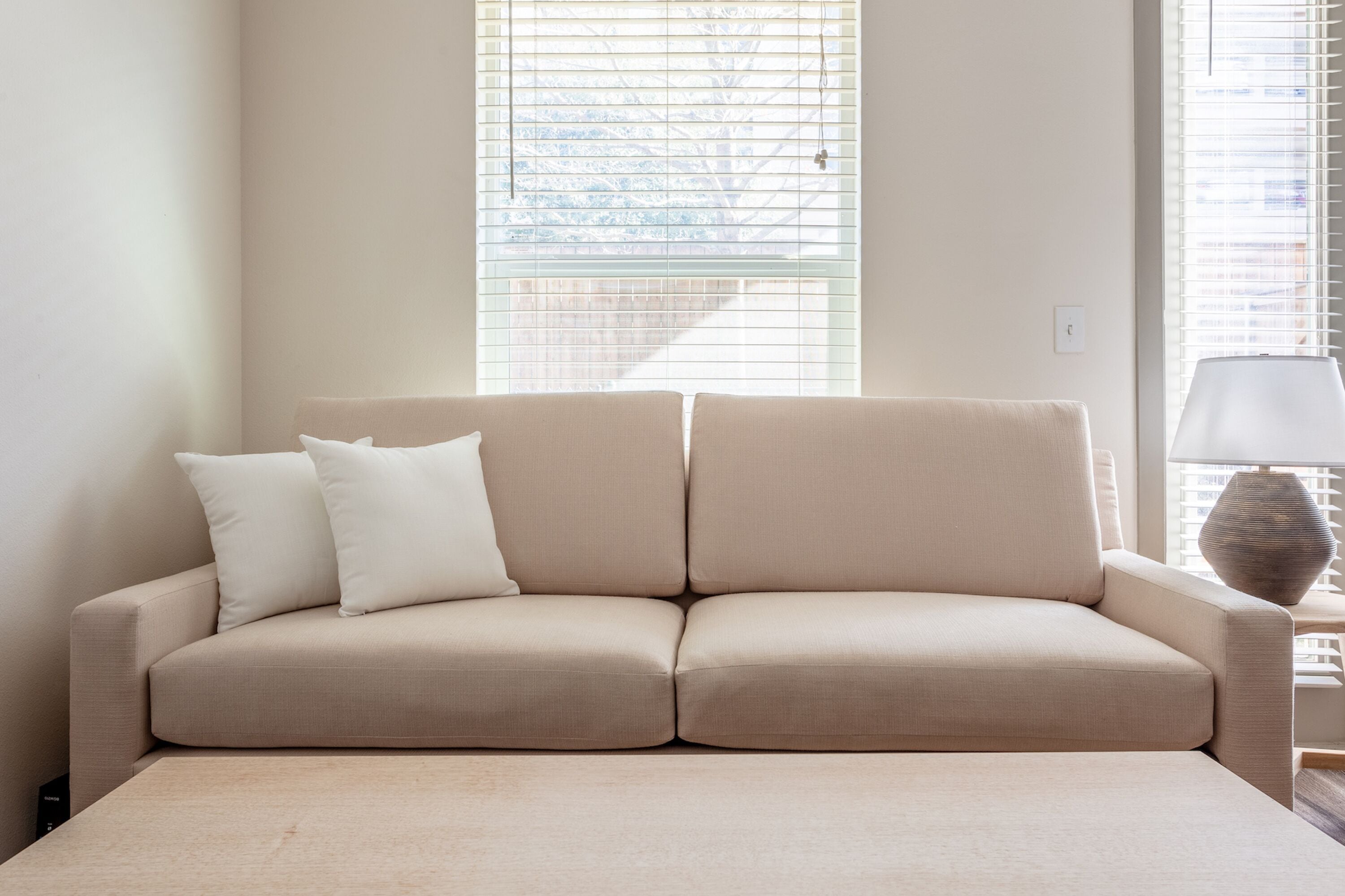 Un sofá beige con dos almohadas frente a una pared con ventana.
