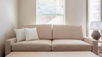 A beige sofa with two pillows against a wall with a window.