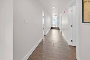 A hallway with white walls and a wooden floor, leading to a set of doors.