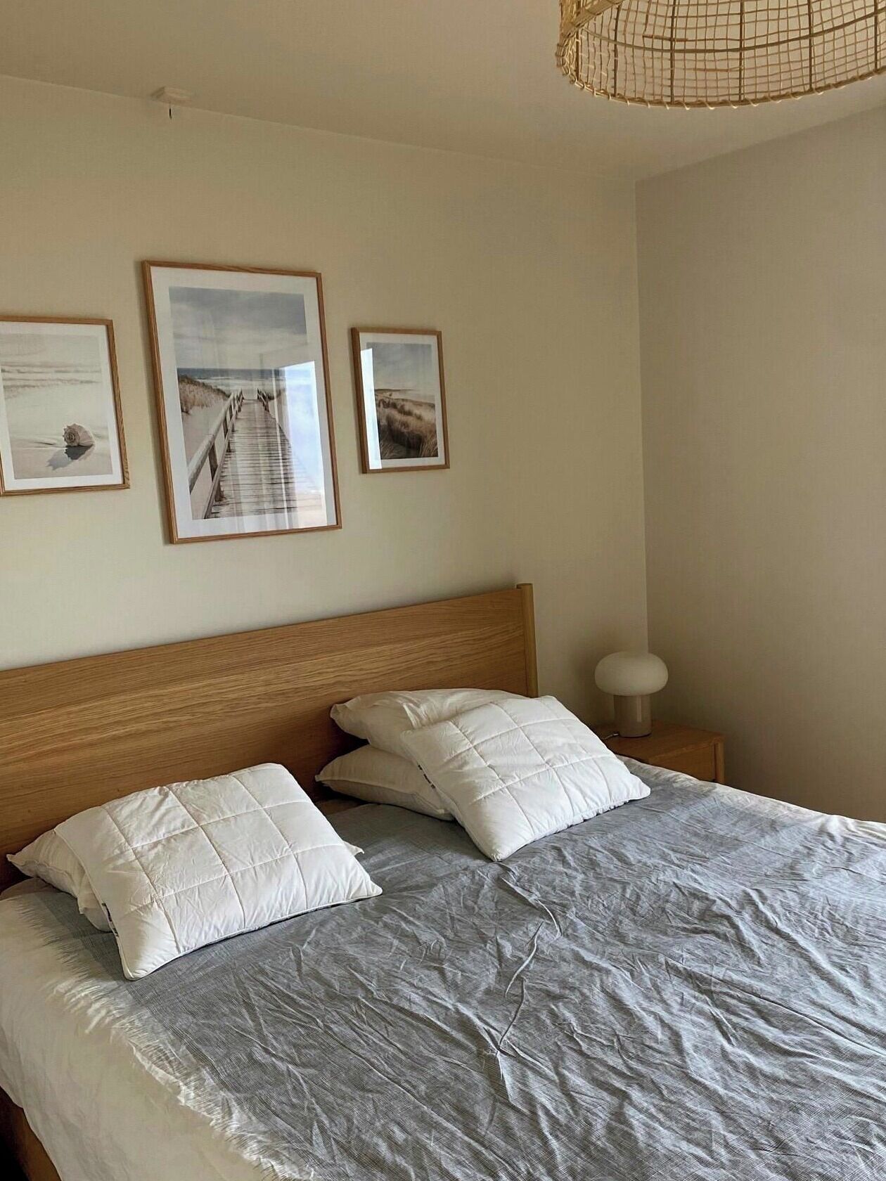 A bedroom with a wooden headboard, a bed with white bedding, and three framed pictures on the wall.