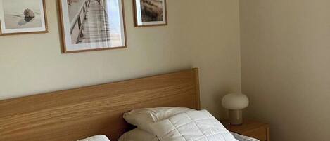 A bedroom with a wooden headboard, a bed with white bedding, and three framed pictures on the wall.