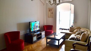 A living room with a television, red chairs, a sofa, and a chandelier. - Exclusive apartment of 120 m2 overlooking the river and free parking (Puerto Madero)