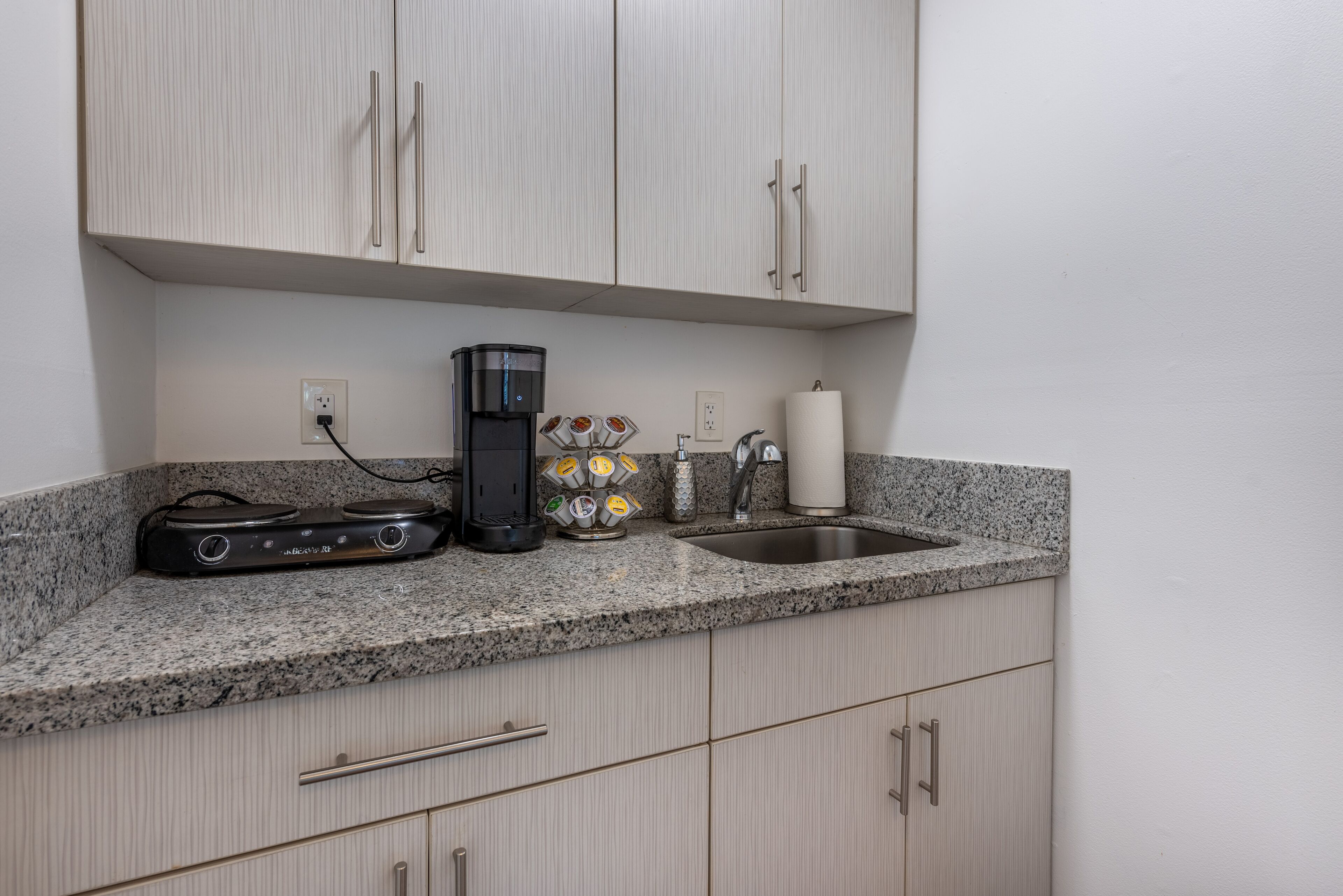 Una cocina con encimeras de granito, cafetera, tostadora, lavabo y un rollo de servilletas de papel.