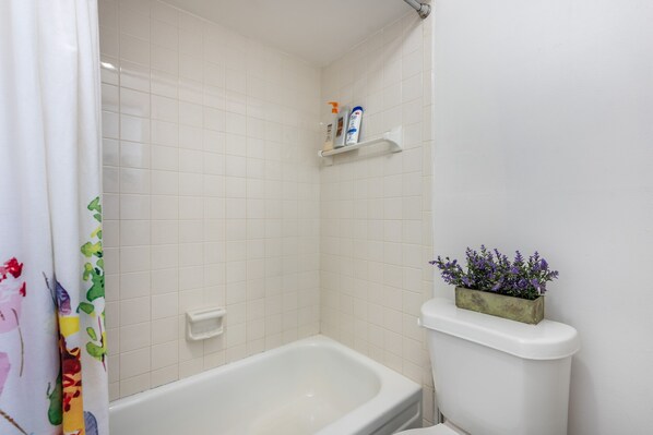 Un baño con una bañera blanca, un inodoro y un estante con artículos de aseo.