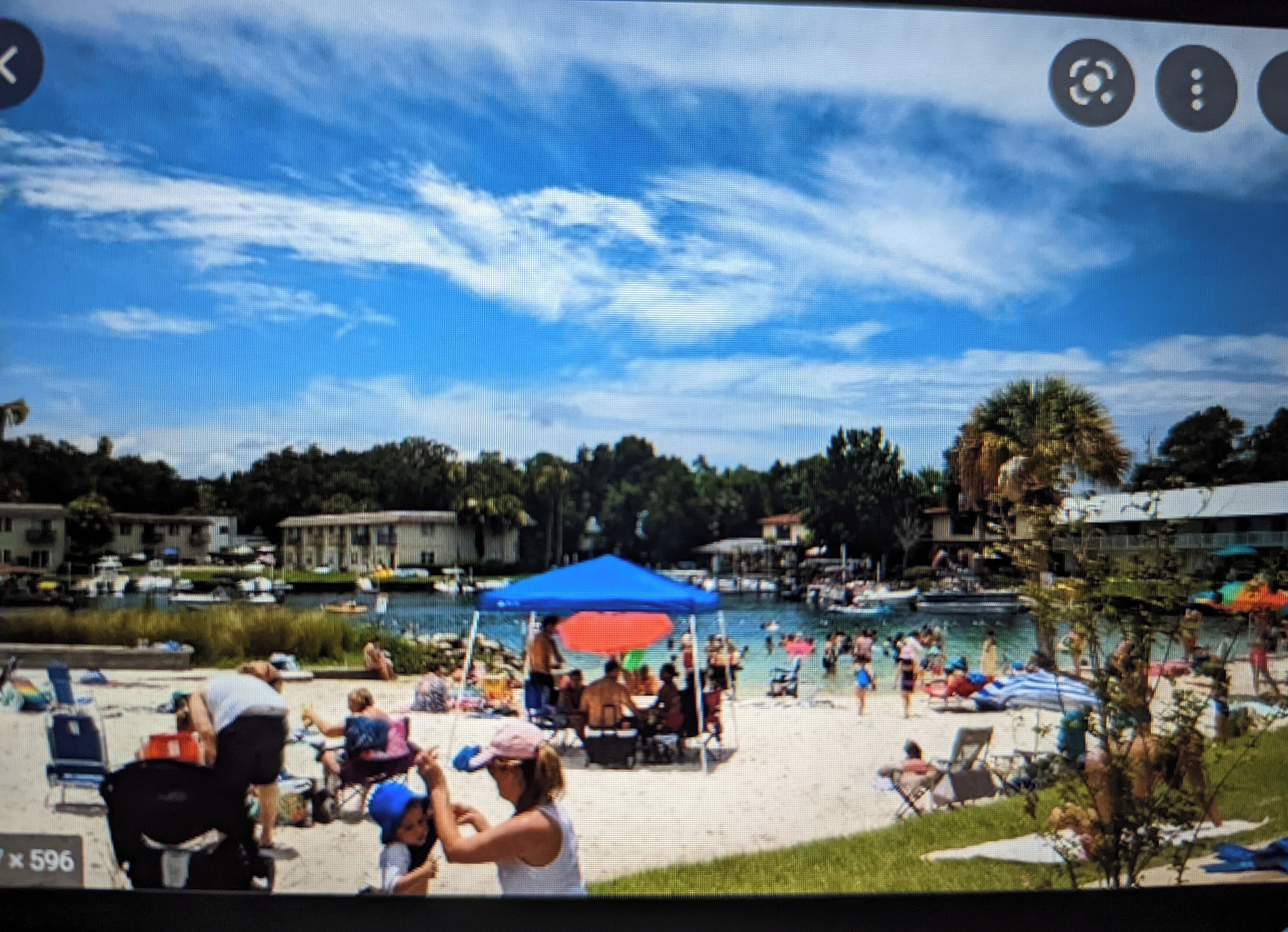 A beach with a pool, umbrellas, and people.