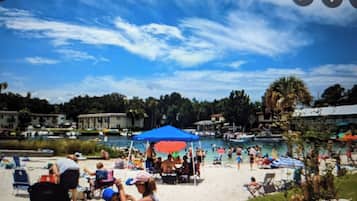 A beach with a pool, umbrellas, and people.