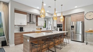 A modern kitchen with a central island, bar stools, stainless steel appliances, and pendant lighting.