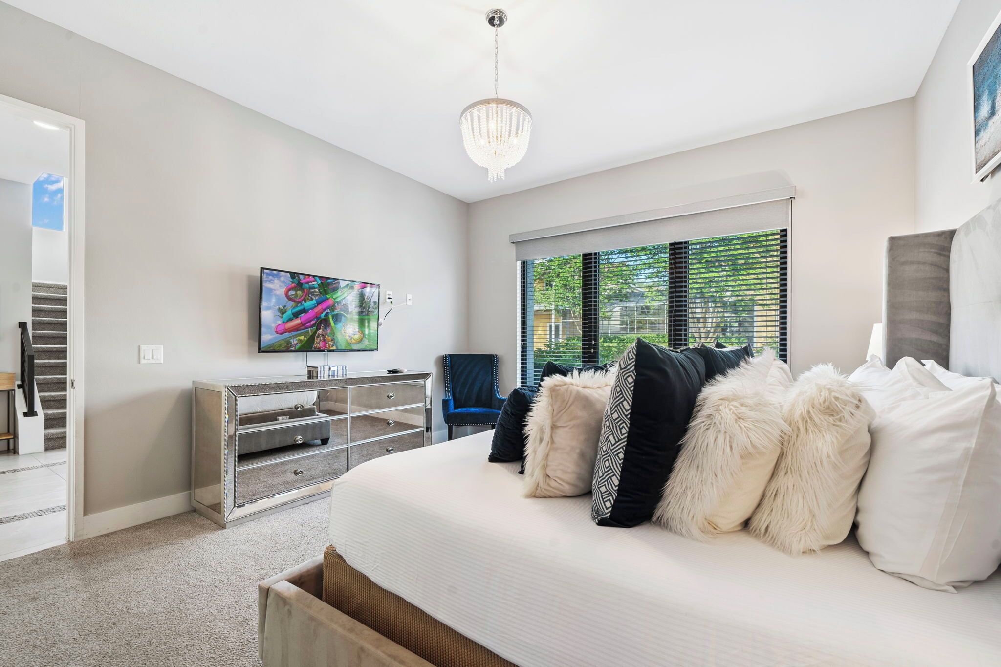 A modern bedroom with a large bed, a TV, and a view of the outdoors through the window.