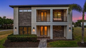 A modern two-story house with a stone facade, a balcony, and a well-maintained lawn.