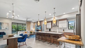 A modern kitchen with a central island, bar stools, pendant lighting, and a view of the outdoors.