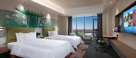 A hotel room with two beds, a desk, a chair, and a large window offering a city view.