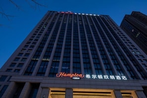 Un edificio de hotel alto con un cartel llamativo de "Hampton" en la base.