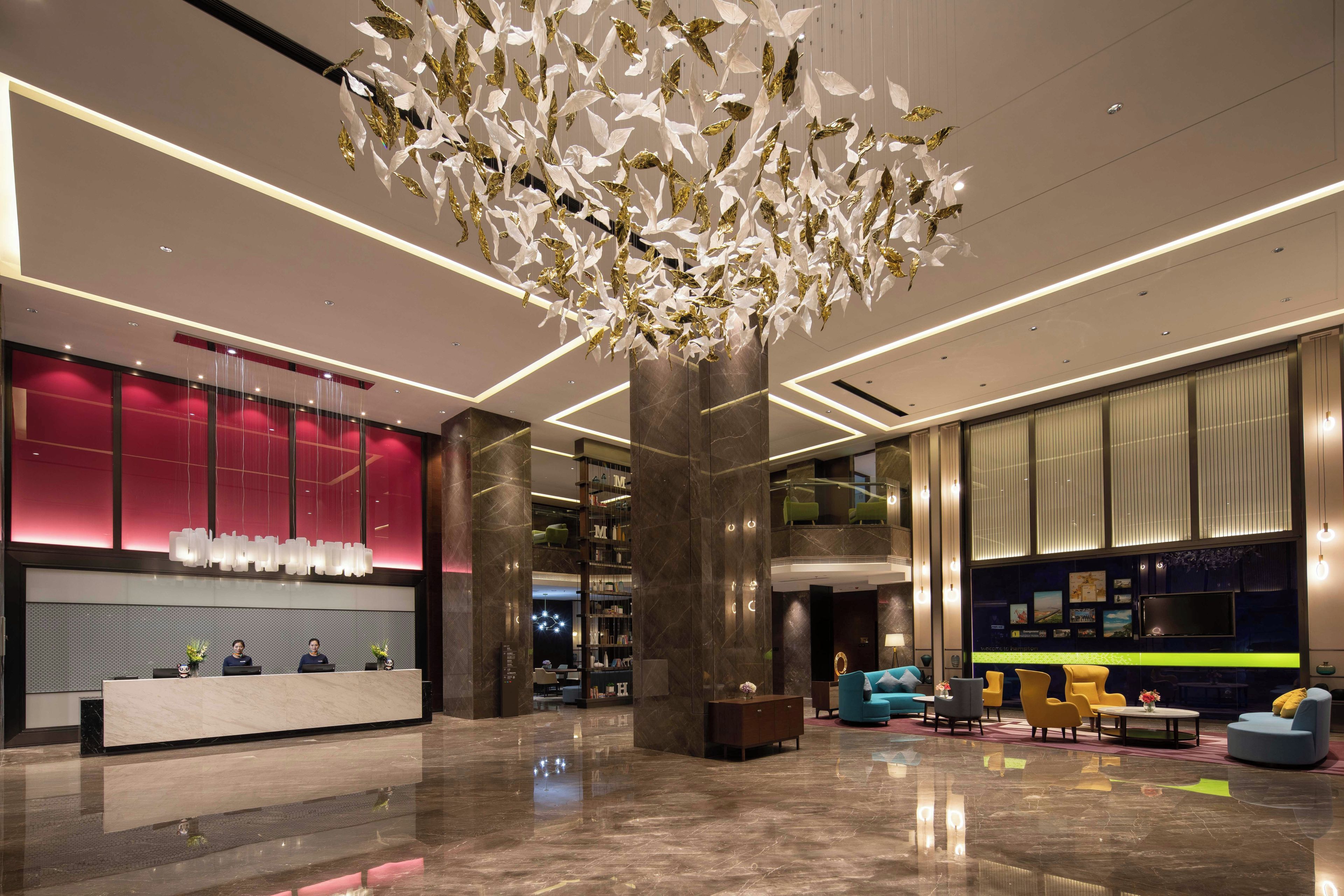 A modern lobby with a reception desk, seating area, and a decorative ceiling installation.