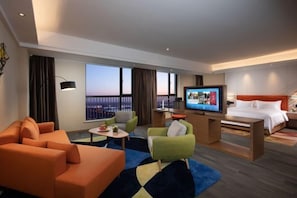 Una habitación de hotel moderna con una cama grande, televisión, escritorio y balcón con vista a la ciudad.
