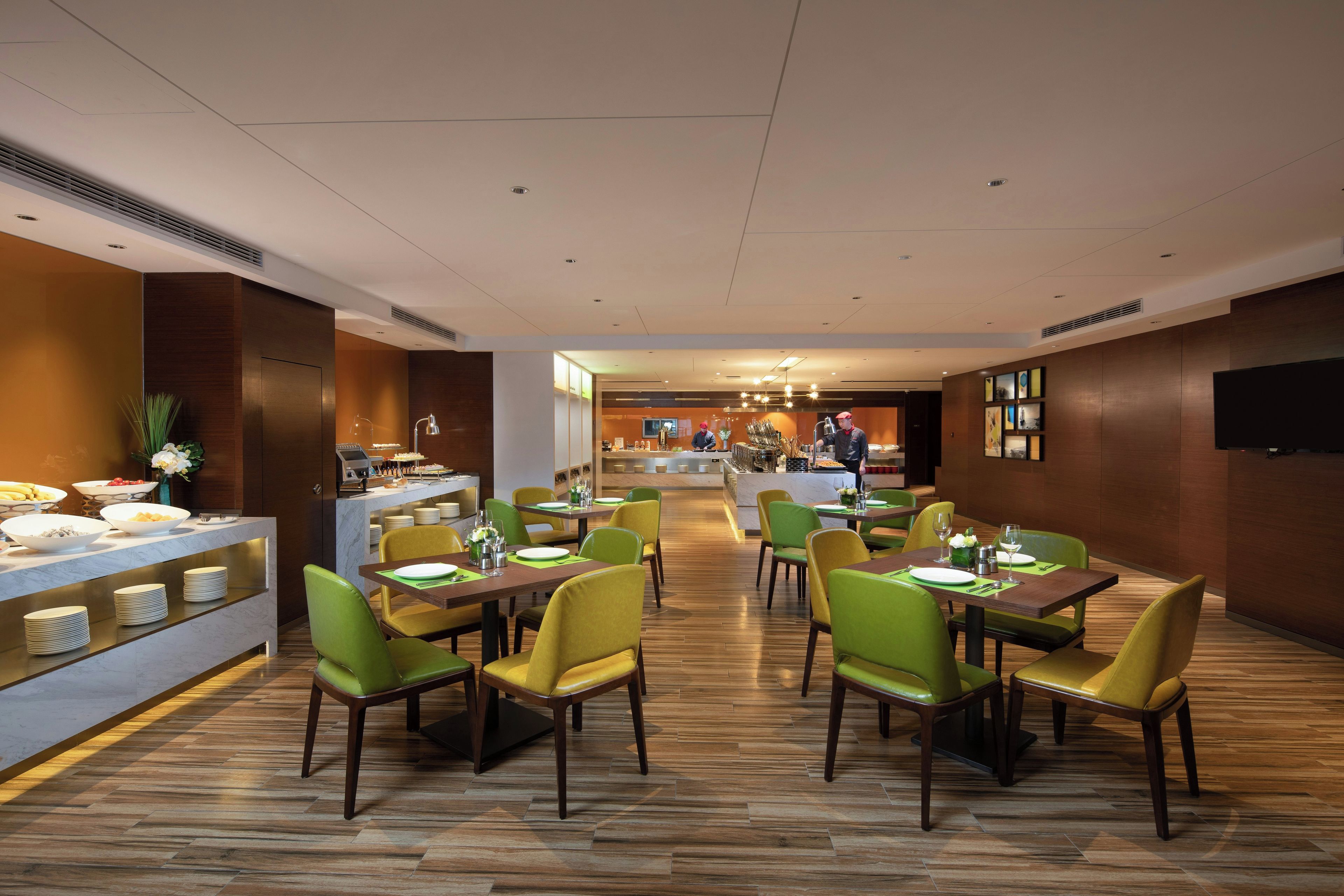 A modern restaurant with a long counter, green and yellow chairs, and a buffet area.