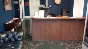 A reception area with a wooden counter, a clock, a fire extinguisher, and a leather chair. - Walton Inn (Willard)