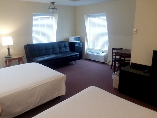 A hotel room with two beds, a sofa, a desk, and an air conditioning unit.
