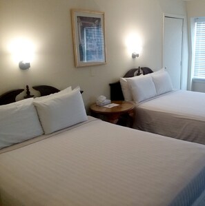 A hotel room with two beds, a small round table, and a framed picture on the wall.