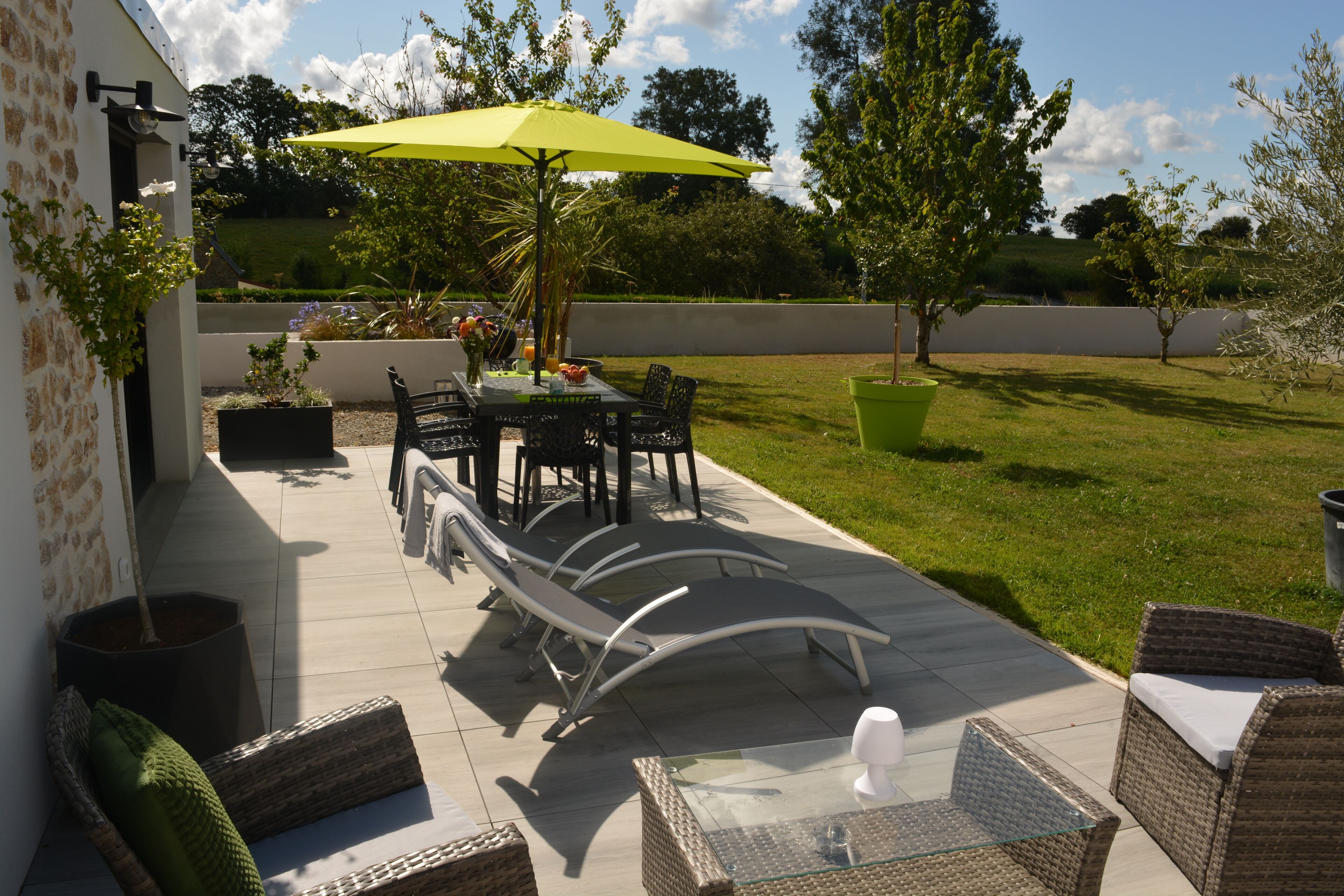 Eine Terrasse im Freien mit Tisch, Stühlen, einem gelben Sonnenschirm und Kübelpflanzen.