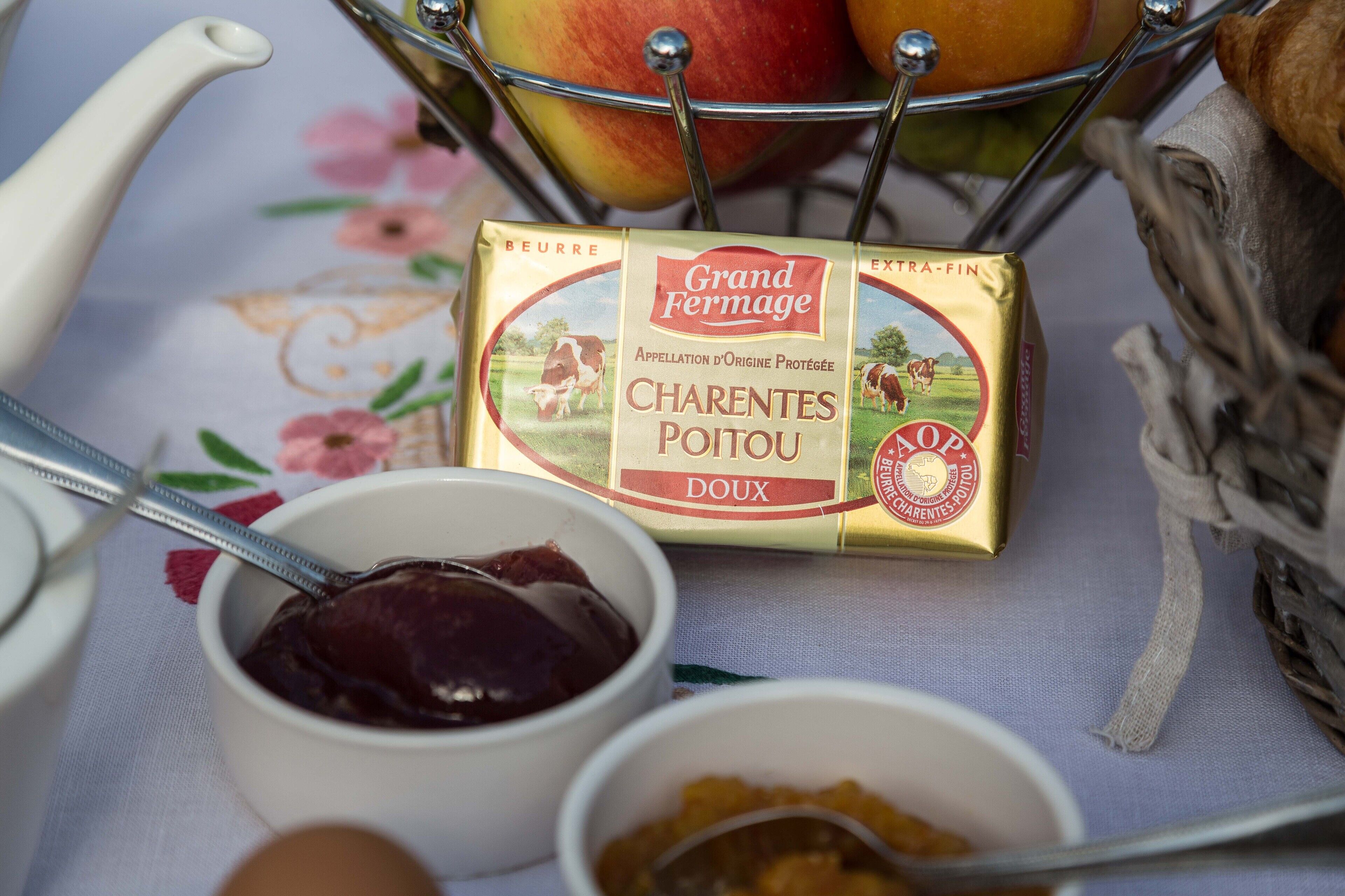 A table setting with a box of Grand Fermage Chârentes Poitou, a bowl of jam, and a basket with apples.
