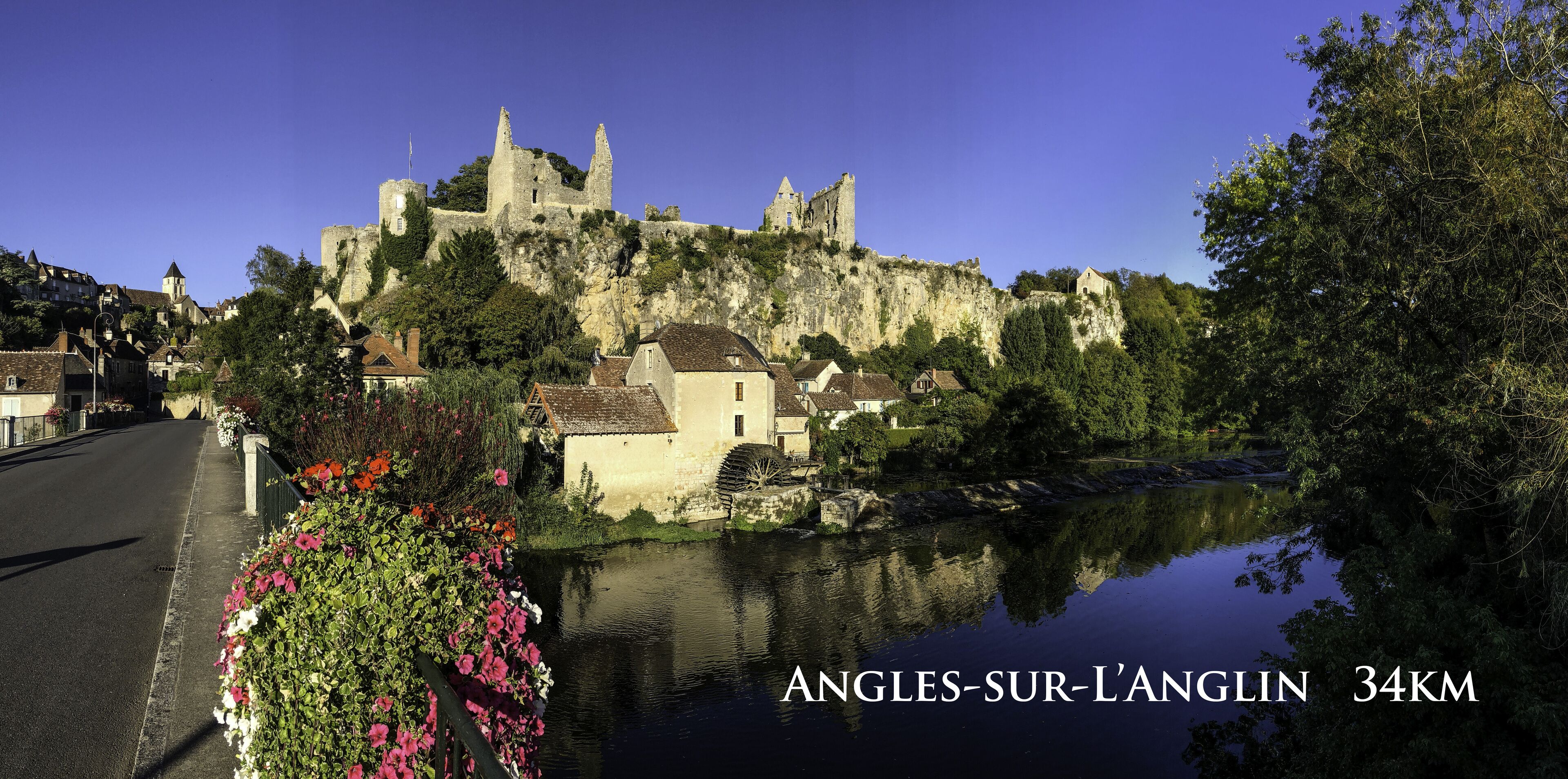 A historic castle on a hill overlooking a town with a river in the foreground.
