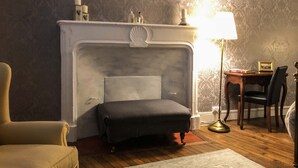 A room with a fireplace, a sofa, a desk with a chair, and a lamp. - La Bicyclette Bleue (Montmorillon)