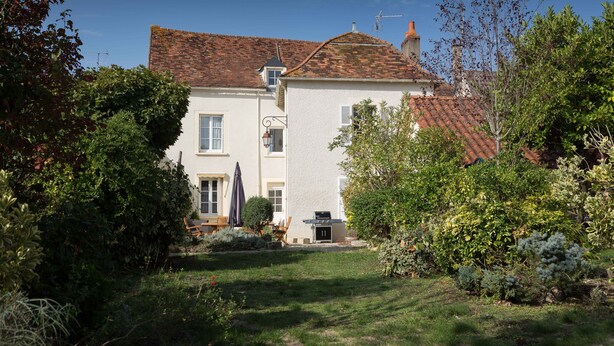 A two-story house with a red-tiled roof, a small attached garage, and a well-maintained garden with various plants and shrubs. - La Bicyclette Bleue (Montmorillon)