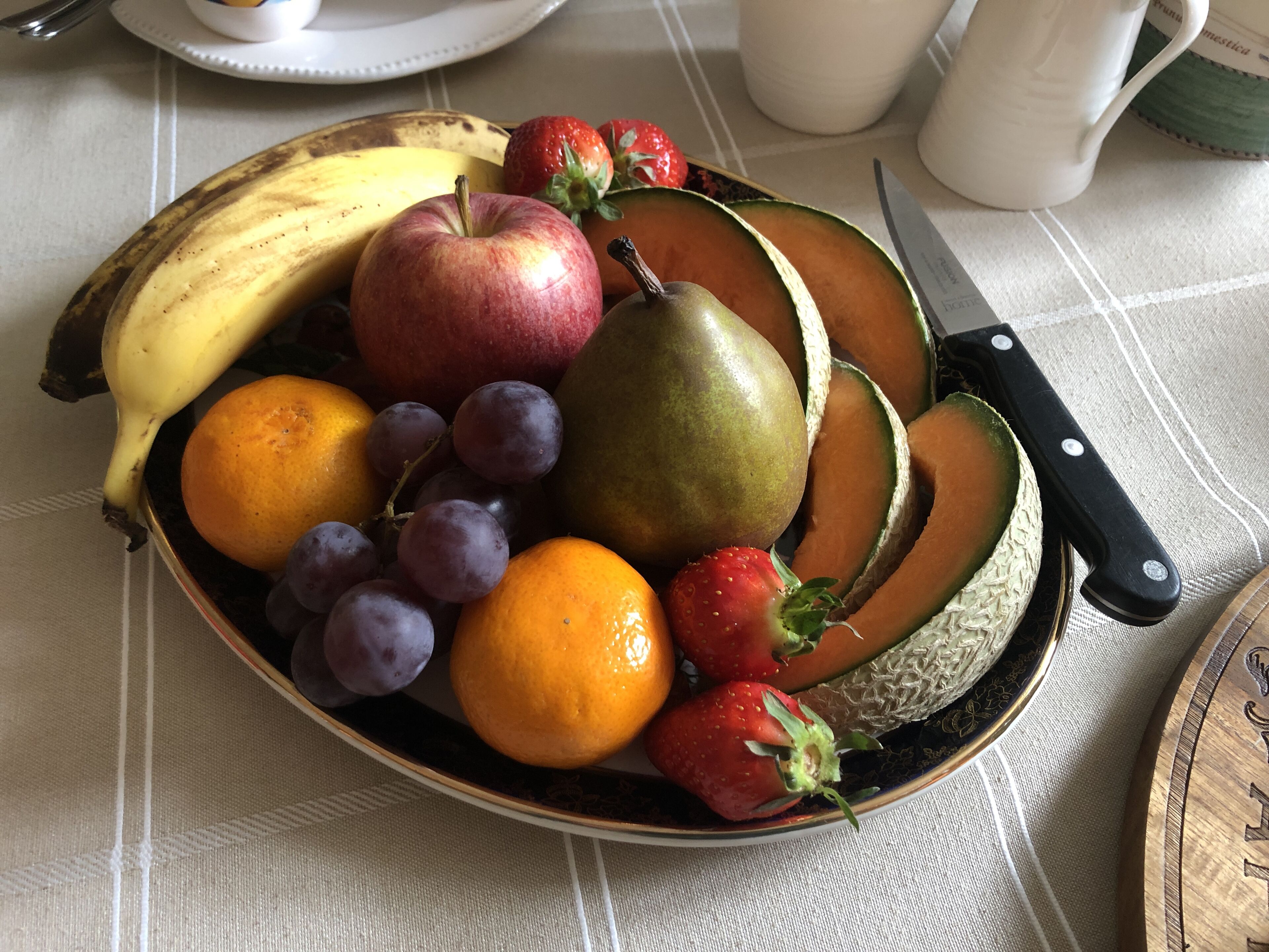 Uma tigela de frutas em cima de uma mesa, com uma faca ao lado.