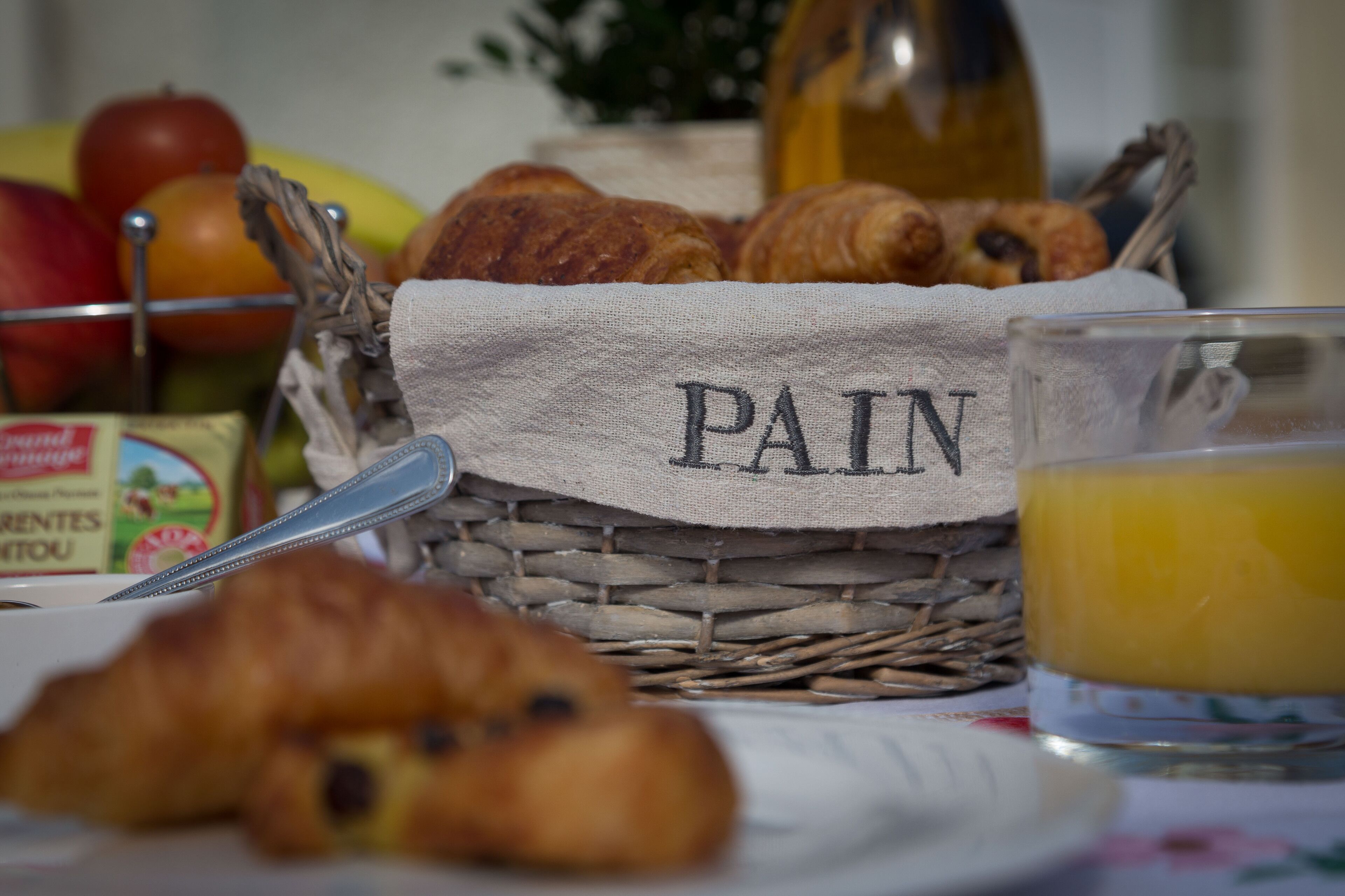 Una cesta con pan y manzanas, un vaso de zumo de naranja y una botella de aceite de oliva.