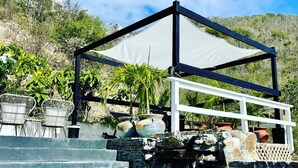 Un área de piscina con vista despejada al agua, una zona de estar cubierta y una ladera en el fondo.