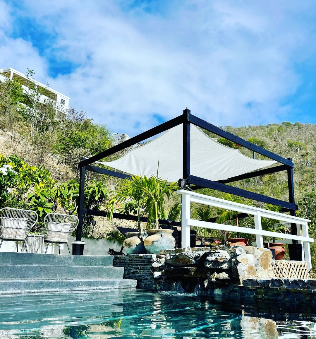 A pool area with a clear view of the water, a covered seating area, and a hillside in the background.