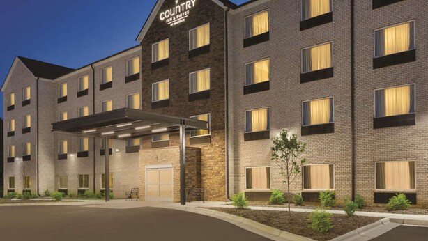 A multi-story hotel with a brick facade, a covered entrance, and a sign indicating it is a country inn and suites. - Country Inn & Suites by Radisson, Greensboro, NC (Greensboro)