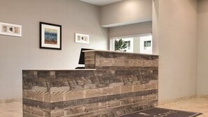 A reception desk with a wooden finish, framed artwork on the wall, and a welcome mat on the floor. - Country Inn & Suites by Radisson, Greensboro, NC (Greensboro)