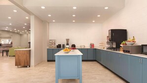 A modern kitchen with a blue island, a refrigerator, and a fruit bowl. - Country Inn & Suites by Radisson, Greensboro, NC (Greensboro)