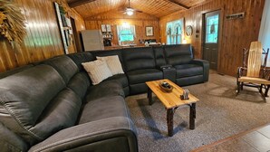 A cozy cabin interior with a sectional sofa, a wooden coffee table, and a dining area with a table and chairs. - Vacation cabin in the beautiful Hocking Hills (Sugar Grove)