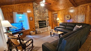 A cozy cabin interior with a stone fireplace, a television, a leather sofa, and a sign that reads "GATHER here". - Vacation cabin in the beautiful Hocking Hills (Sugar Grove)