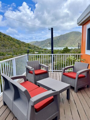 A deck with wicker furniture and red cushions, overlooking a mountainous landscape with a body of water. - "Caribbean" 1 Bedroom in The Garden of Eden (st. john)