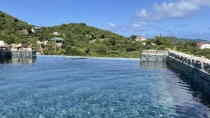 Une piscine aux eaux cristallines, bordée de pierres, entourée d’une végétation luxuriante et avec des collines en arrière-plan.