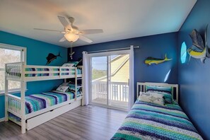 A room with two bunk beds, a ceiling fan, and a large window with a view of the outdoors. - "Always Sunny" Beautifully Remodeled Home, Quick Walk to Beach (Surf City)