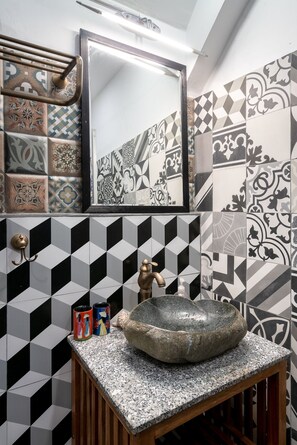 Bathroom features a geometric tile pattern, a large stone sink, and a gold faucet.