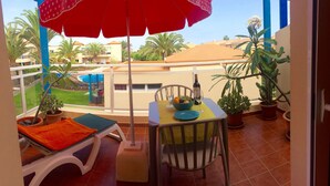 A balcony with a table, chairs, a red umbrella, and potted plants.