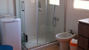 A bathroom with a glass-enclosed shower, a white sink, a bidet, and an orange rug.