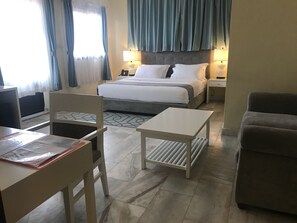 A hotel room with a bed, two bedside tables, a desk, a chair, and a sofa. - Sunset Inn Guest House (Monrovia)